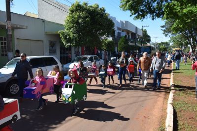 NA SEMANA DO TRÂNSITO, ALUNOS DA EDUCAÇÃO INFANTIL DESFILAM NA AVENIDA PRINCIPAL COM CARRINHOS DE PAPELÃO.